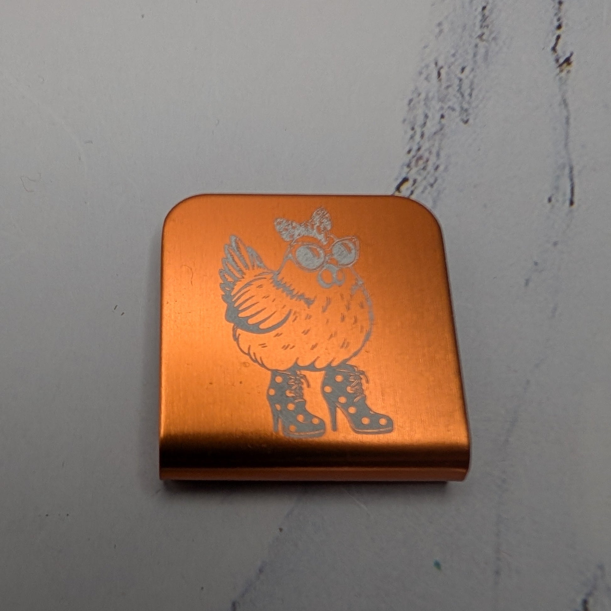 Orange  hat clip with a chicken character on a marble surface