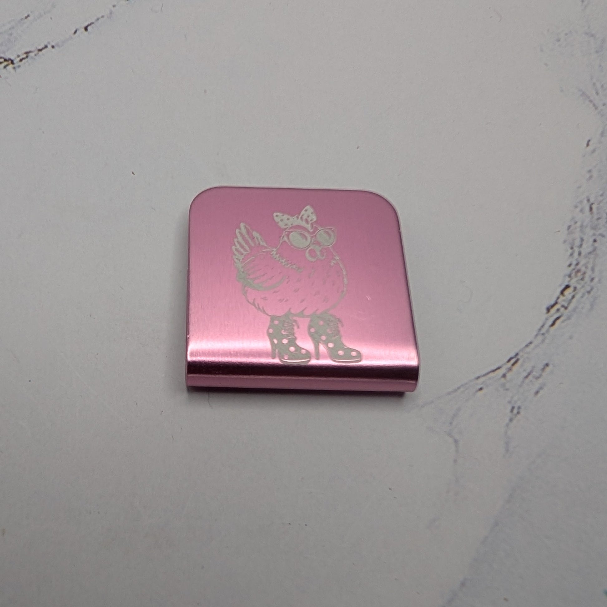 Pink  hat clip with a chicken character on a marble surface