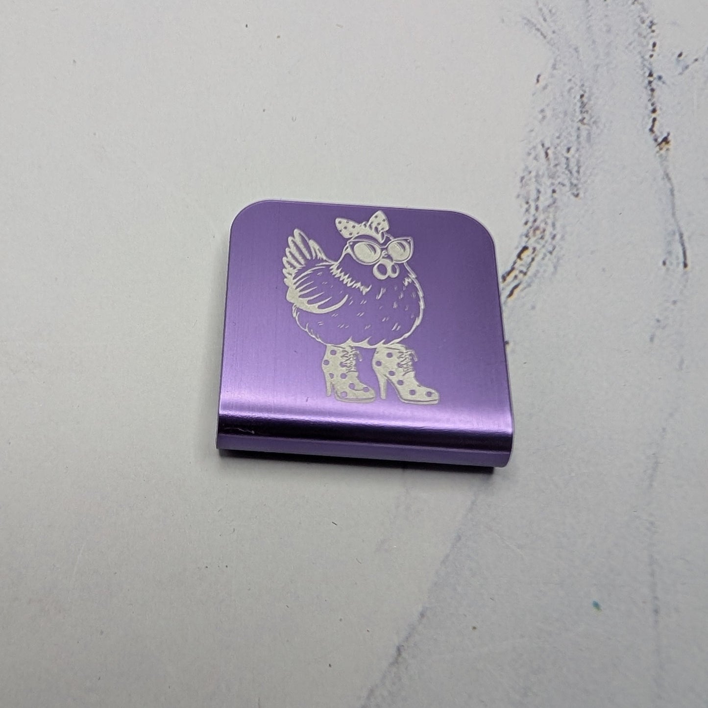 Purple hat clip with a chicken character on a marble surface
