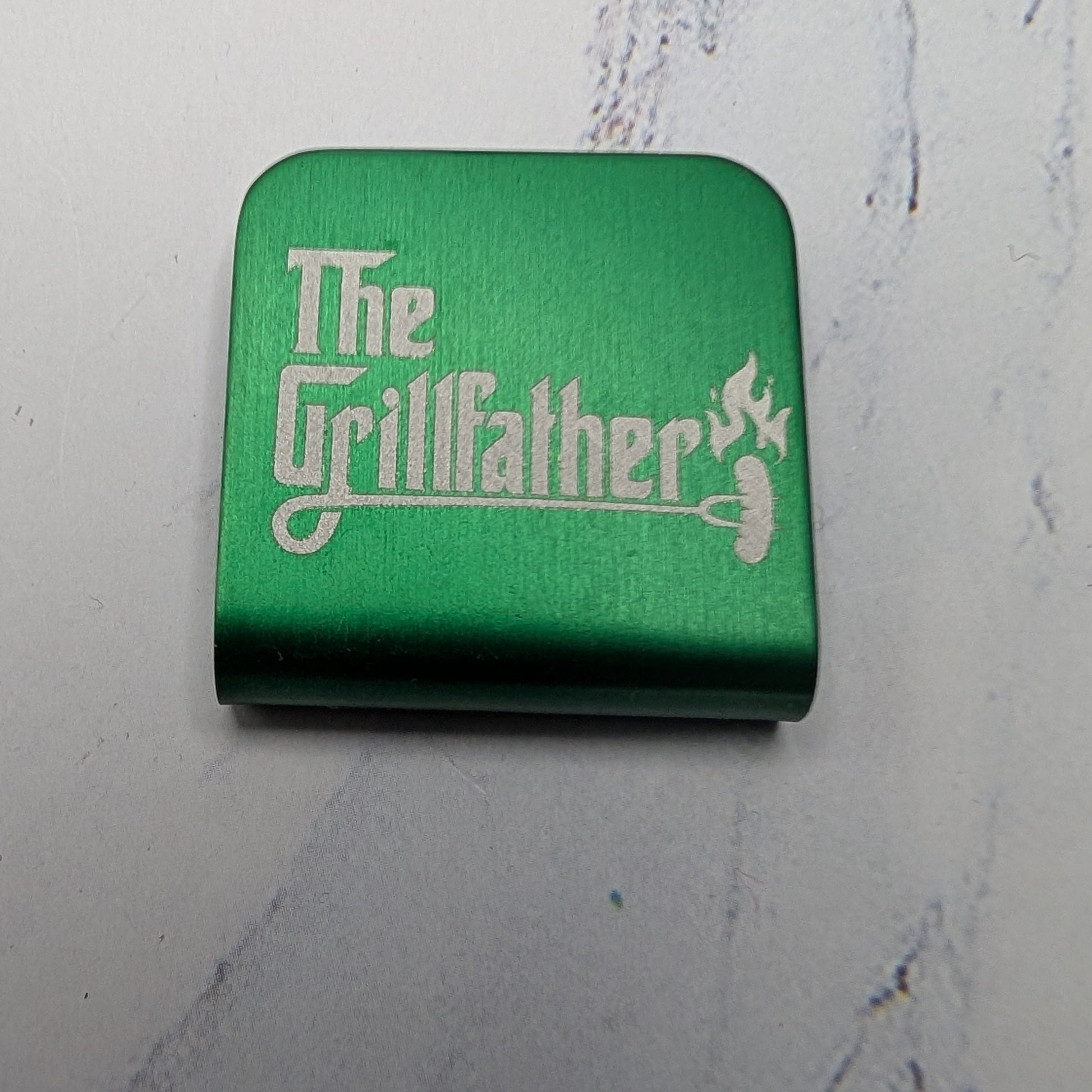 Green hat clip with 'The Grillfather' text on a marble surface