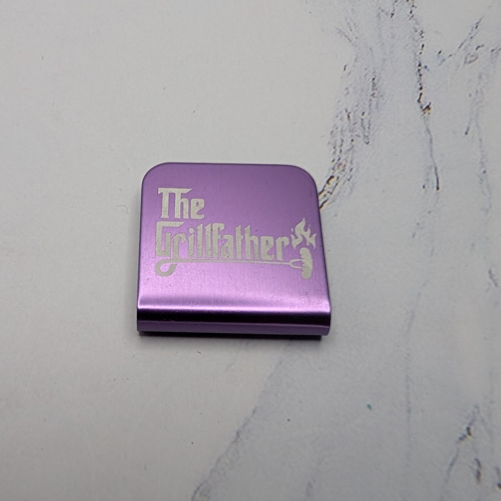 Purple hat clip with 'The Grillfather' branding on a marble surface